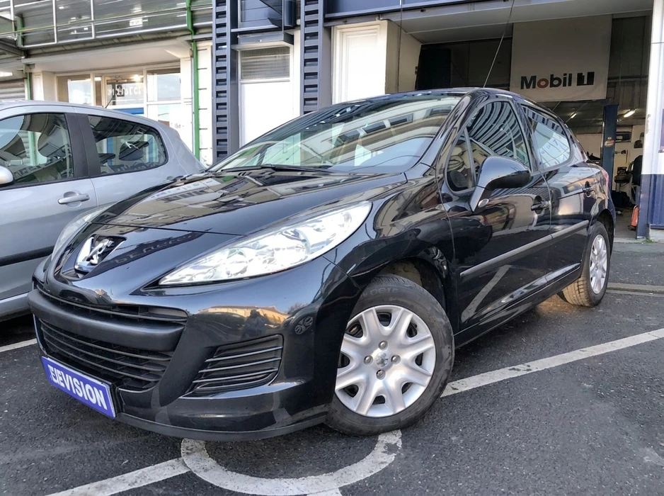 Véhicule Peugeot 207 berline 5 portes, coloris noir brillant, stationné devant un garage automobile avec enseigne Mobil 1