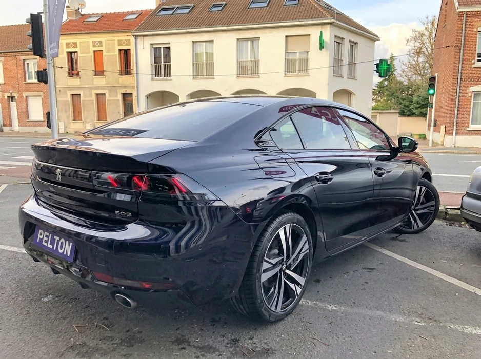 Véhicule Peugeot 508 berline fastback noir métallisé, vue arrière trois quarts, stationnée en milieu urbain français