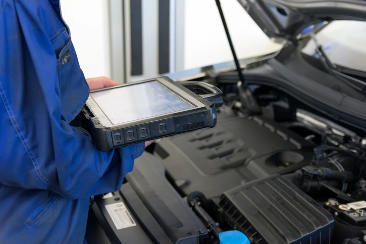 Photographie d'un client dans l'espace d'accueil du garage Lenica, en conversation avec un mécanicien ou un responsable d'atelier. Le client est au premier plan, en train de discuter du diagnostic de son véhicule ou de la maintenance de sa voiture. L'arrière-plan montre un atelier automobile professionnel avec des outils et des véhicules visibles, créant une atmosphère de confiance et de savoir-faire. L'image doit transmettre une relation client personnalisée et professionnelle.