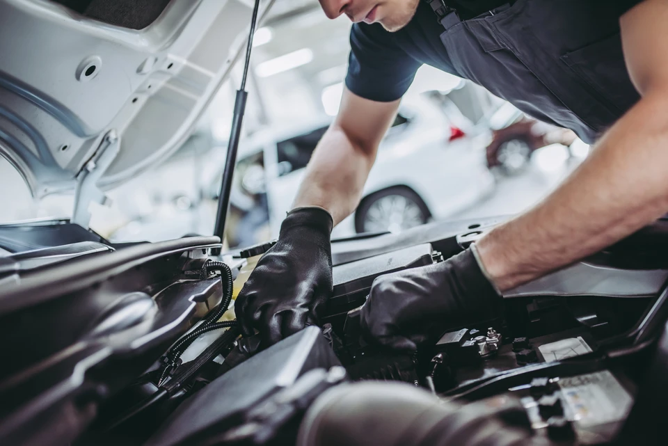 Mécanicien automobile inspectant un moteur ouvert, tenant un carnet de maintenance avec grille de contrôle technique